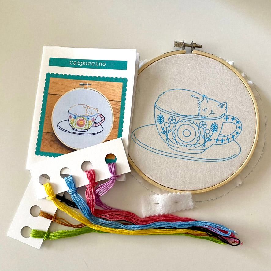 Catpuccino embroidery kit with bamboo hoop, fabric, thread, and instructions featuring a cat-themed design.
