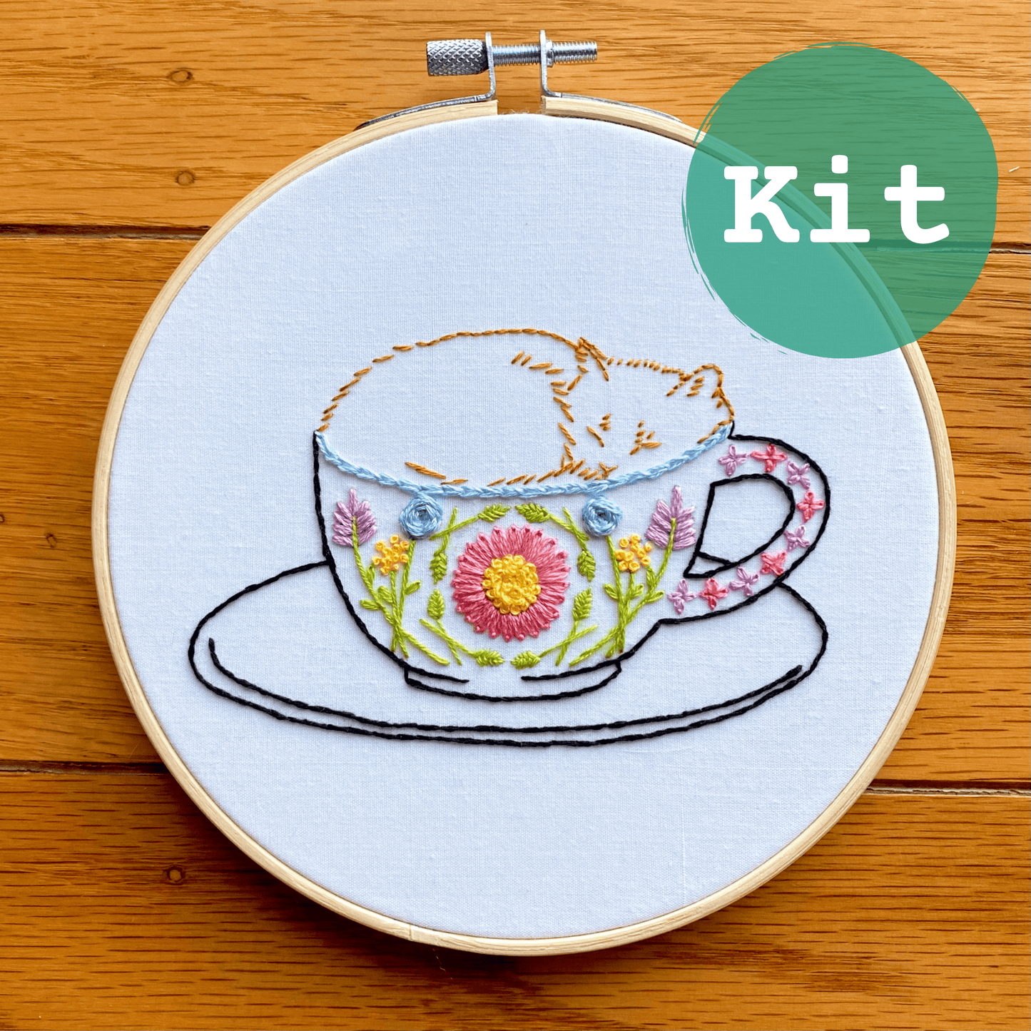 Catpuccino embroidery kit with a sleepy cat in a floral mug on a hoop.