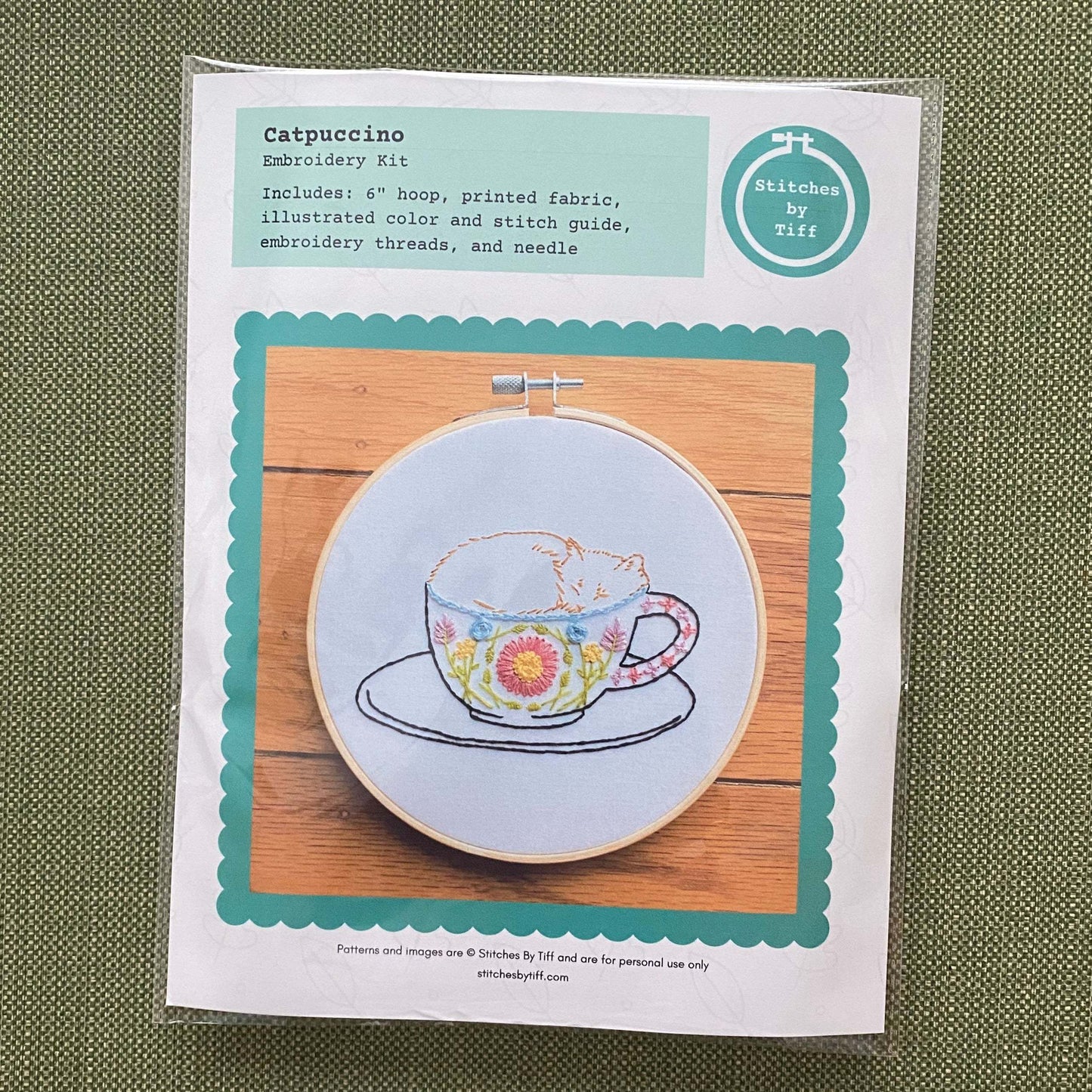 Catpuccino embroidery kit with hoop, fabric, and colorful threads featuring a cat in a floral mug design.