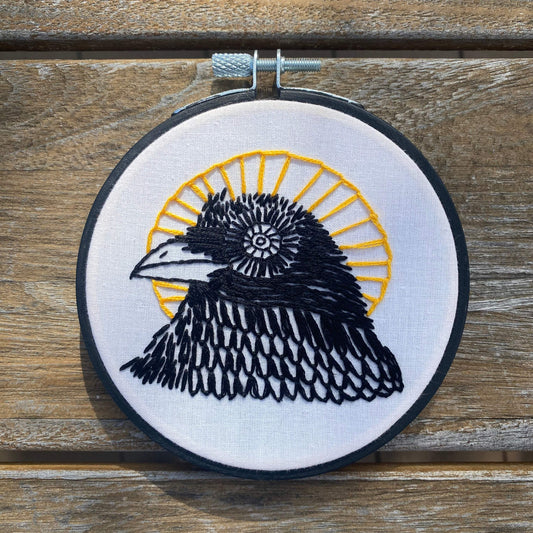 Black bird with sun halo embroidery kit on white fabric in a 4-inch hoop.