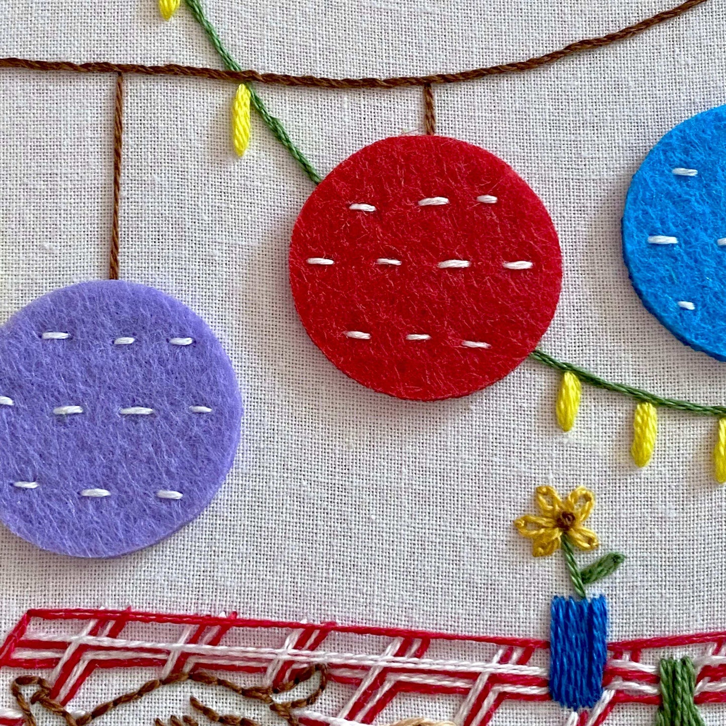 Colorful picnic-themed embroidery featuring felt circles and textured stitches on fabric with hanging lanterns.