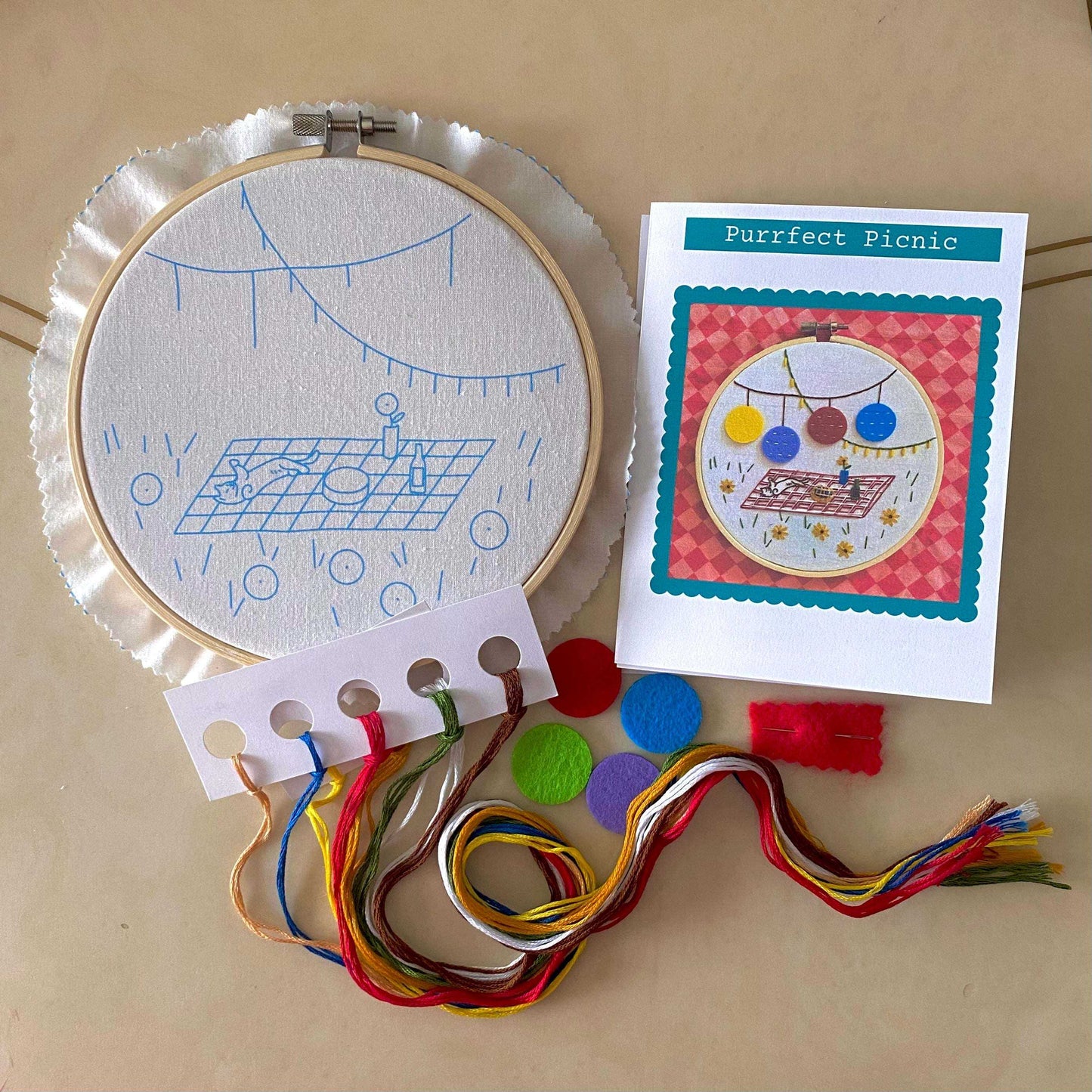 Picnic themed embroidery kit with hoop, pre-printed fabric, colorful threads, and instructions for various stitches.