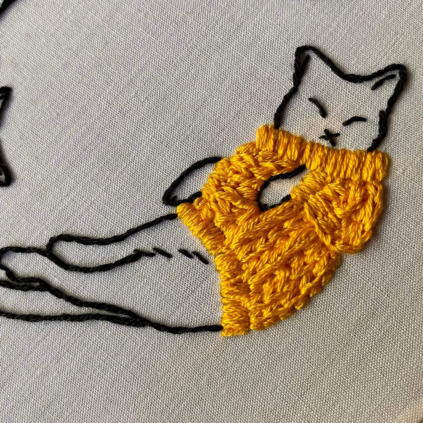 Embroidery of a cat in a cozy sweater using various stitches on white fabric.