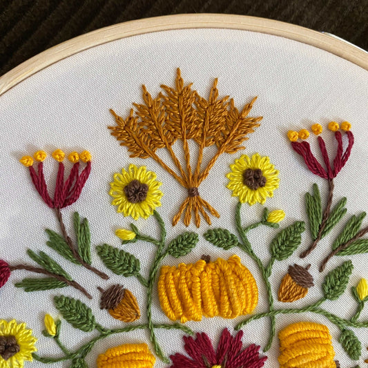 Autumn-themed mandala embroidery in progress with fall motifs in a bamboo hoop.