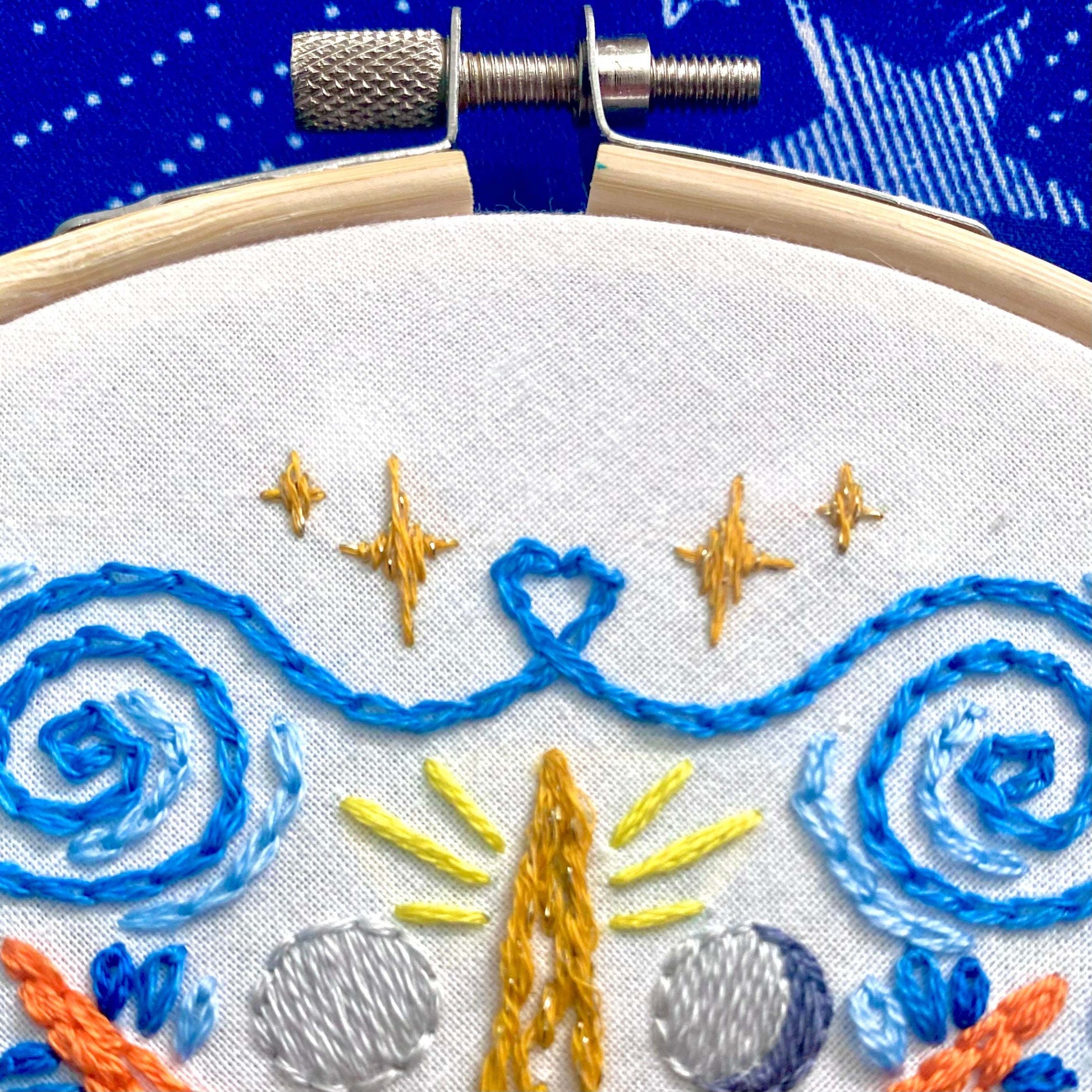 Celestial Mandala Embroidery Kit with bamboo hoop, colorful stitched sun, moon, stars, and sparkly thread on white fabric.