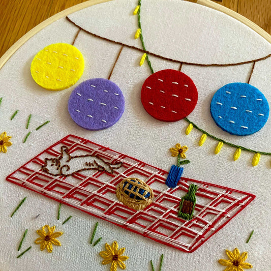 Picnic-themed embroidery kit with colorful felt lanterns and textured stitches in a hoop.